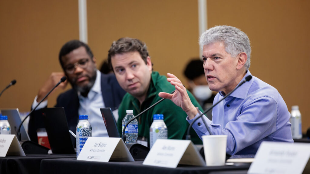 Three advisory committee members seated at a conference table during a George Shultz Innovation Fund finalist presentation.